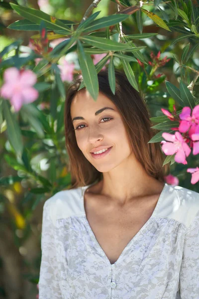 Vakker kvinne med perfekt hud og sjarmerende smil nær blomstrende rosa blomster i hagen – stockfoto
