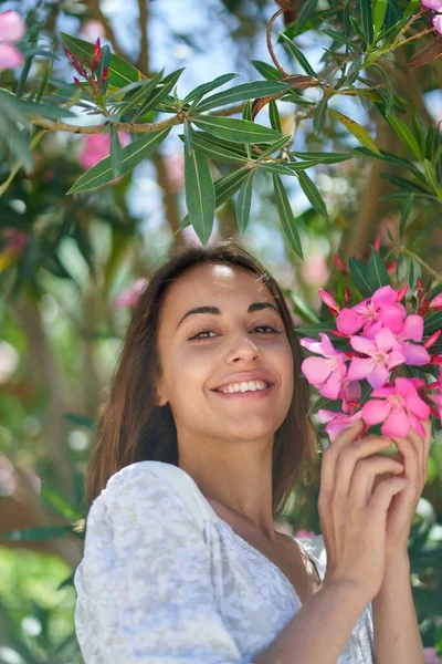 Vakker latinakvinne som smiler til kamera, tar på rosa blomster i hagen. – stockfoto