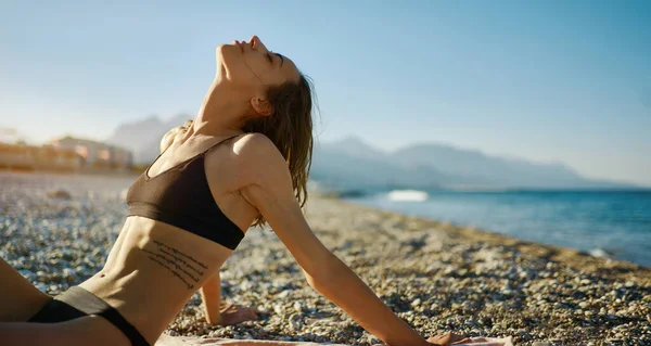 Widok z boku piękna kobieta model w bikini pozowanie na plaży morskiej podczas zachodu słońca z górami na tle — Zdjęcie stockowe