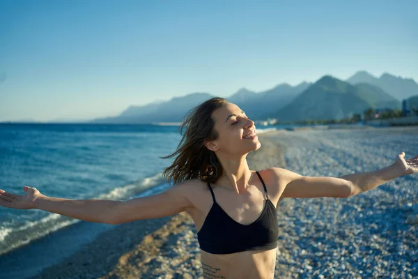 Libertad mujer de pie contra el cielo azul y las montañas en la playa con los brazos abiertos — Foto de Stock