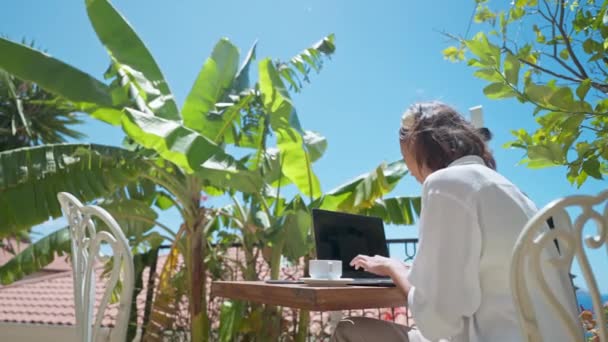 リアビューフリーランスの女性は、屋外バルコニー旅行ホテルから地中海の景色の上に白い空の画面とラップトップコンピュータ上で作業. — ストック動画