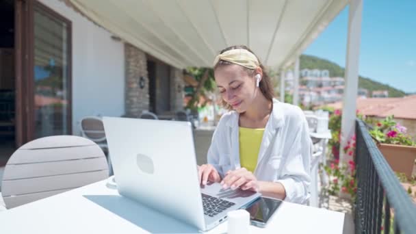 海の景色が美しい白いオープンテラスでラップトップで屋外で働く若い女性実業家,トルコの夏休みの間に働くリモートオンライン, 4kスローモーション. — ストック動画