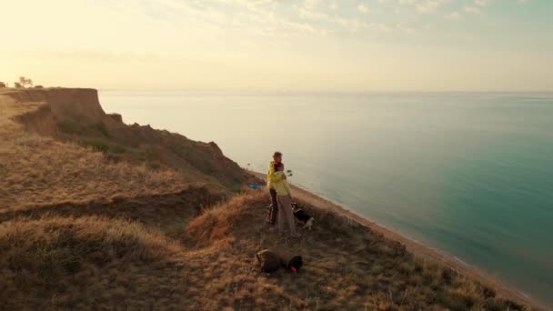 Casal feliz com cão em pé na borda do penhasco e desfrutando de uma vista incrível acima da água do mar — Vídeo de Stock