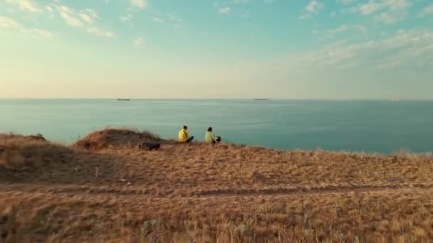 Dos viajeros con perro sentado en el borde del acantilado y con vistas al Mar Negro. Yuzhne, región de Odessa, Ucrania. — Vídeo de stock