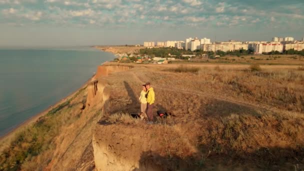 Pareja feliz con perro de pie en el borde del acantilado y disfrutando de una vista increíble sobre el agua de mar — Vídeos de Stock