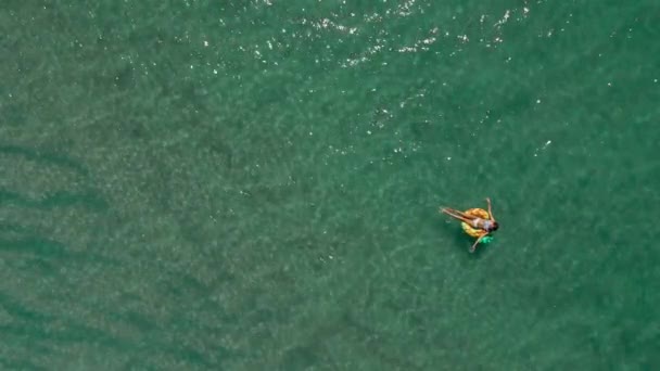 Vista aerea dall'alto dell'acqua turchese del mare e della donna che nuota sull'anello di nuoto giallo. Filmati panoramici del paesaggio marino estivo. — Video Stock