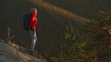 Kırmızı ceketli ve bereli gülümseyen genç bir kadının portresi. Kız gün batımında dağın tepesinde doğa yürüyüşü yaparken kendinden emin ve mutlu görünüyor. Ukrayna 'daki Karpat Dağları.