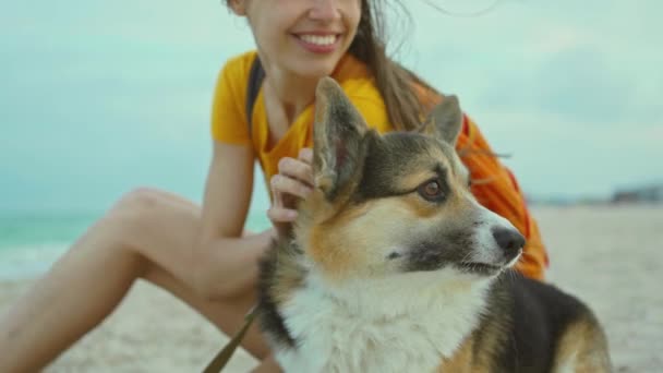 Atraente jovem mulher sorrindo e passar o tempo em conjunto com seu animal de estimação bonito corgi cão ao ar livre na praia do mar arenoso ao pôr do sol. — Vídeo de Stock
