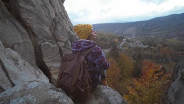 De meidenwandelaar zit aan de rand van de klif en kijkt in de verte, uitzicht op de bergen, reizen en sport. Beroemde toeristische plaats in Oekraïne, Tustan National Park — Stockvideo