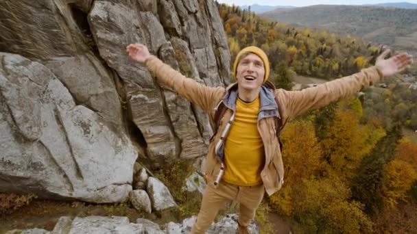 Hombre feliz excursionista con mochila relajarse en la parte superior de un acantilado y disfrutar de la vista del valle de Tustán, Ucrania. sonriente hombre se para con las manos levantadas y se siente libre y feliz. — Vídeo de stock