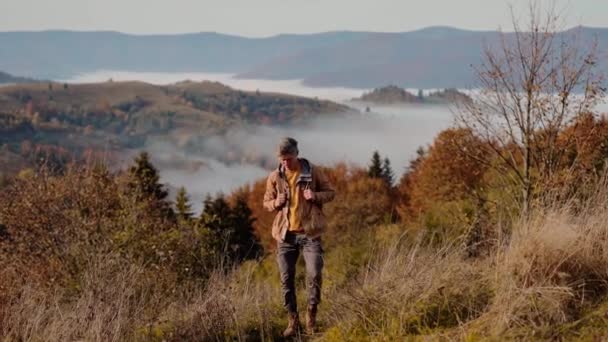Erkek hippi maceracı sabahın erken saatlerinde dağ geçidinde yürüyor, etrafa bakıyor, güzel manzaranın tadını çıkarıyor, mutlu oluyor ve güneşin doğuşunu selamlıyor. Ukrayna, Karpat dağlarında insan yürüyüşçüsü. — Stok video