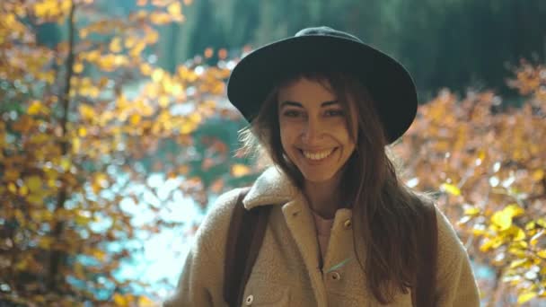 Closeup cheerful ukrainian Woman tourist on trail in fall forest on sunny autumn day. female hiker in hat with backpack hiking in forest around mountain lake Sinevir at cold autumn morning, Ukraine. — Vídeos de Stock