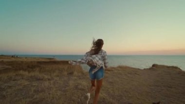 Yavaş çekimde, gün batımında panoramik manzarayla tepenin üstünde koşan mutlu esmer kız. Güzel, keyifli bir kadın doğadaki macerasından zevk alıyor.