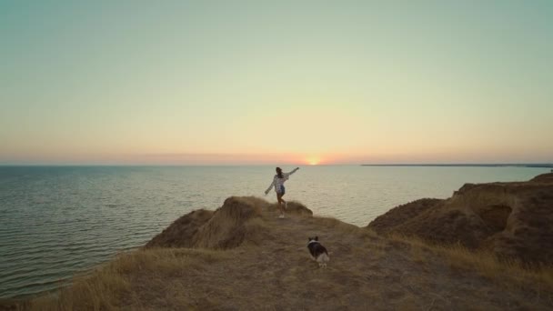 Slow motion Back view happy brunette blowing hair woman running by hill top with panoramic view at sunset. beautiful girl enjoying her adventure in Ukraine with her per welsh corgi dog — Stok video