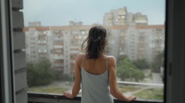 Evde balkonda duran genç bir kadının arkadan görünüşü, yavaş çekim, sosyal mesafeler ve karantina tecridi. Depresyon ve akıl hastalığı, intihar düşünceleri