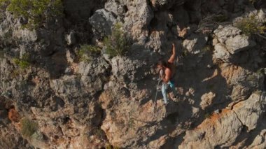 Güçlü kaslı bir adamın hava aracının havadan bakış açısı kaya tırmanışı rotasını zorluyor. Tırmanışçı tutamaklara ulaşır ve uzun sert bir hamle yapar