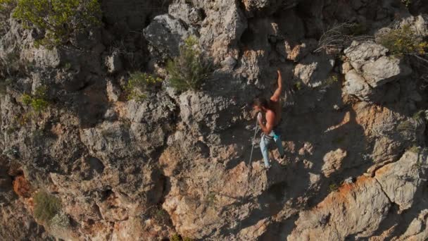 Punto di vista aereo da drone di forte uomo muscoloso sale impegnativa via di arrampicata su roccia. arrampicatore raggiunge le maniglie e fa una lunga mossa difficile — Video Stock