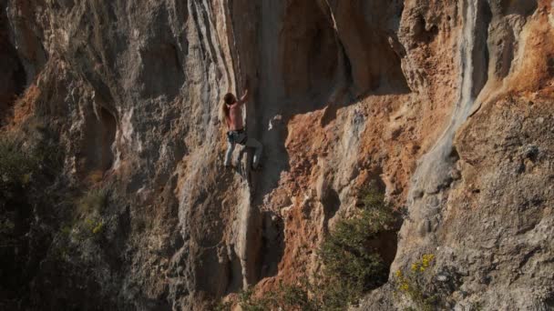 Zpomalený letecký dron záběry silného muže skalního horolezce šplhající na tvrdou cestu na svislé útesu s obrovským tufou. horolezec dělá několik obtížných snah a pohybů udržet — Stock video