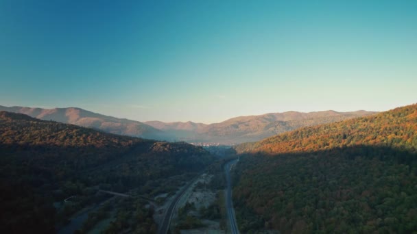 Voo drone aéreo cinematográfico sobre vala de montanha nebulosa com estrada e ferrovia para Skole, pequena cidade nas montanhas dos Cárpatos, Ucrânia. destino de viagem e transporte. — Vídeo de Stock