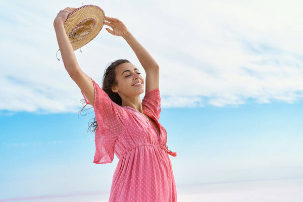 Portrait carefree pleased woman in pink dress holding hat over head on blue sky background Royalty Free Stock Photos