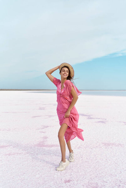 Elegant woman on salt beach at pink lake. Girl in hat and pink dress blowing feeling breezy air Stock Picture