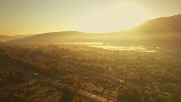 Vista aerea cinematografica fro drone su strada con veicoli merci e ferrovie all'alba soleggiata nella valle di montagna in Carpazi, Ucraina occidentale. Trasporto e consegna del carico. — Video Stock