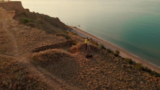 Glada par med hund står på kanten av klippan och njuter av fantastisk utsikt över havet vatten — Stockvideo