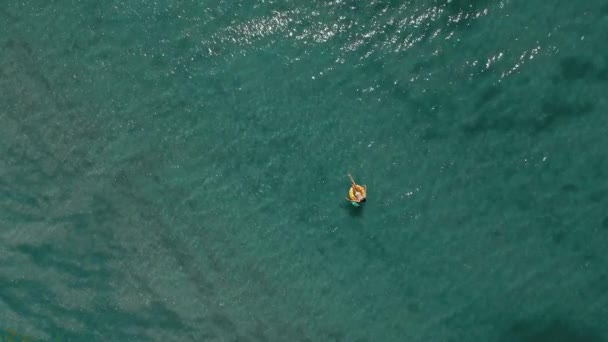 공중 드론 정상에서 청록색 해수와 편안 한 여자가 노란 떠 있는 수영 고리를 타고 헤엄치고 있는 모습. 여름 풍경의 파노라마 영상. — 비디오