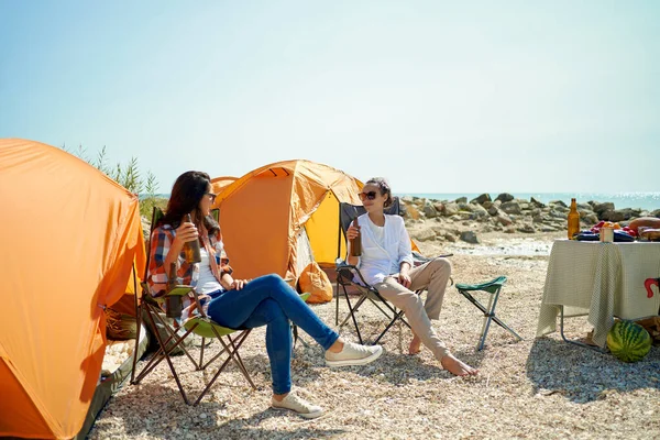Kaksi naista ystäviä juo kylmää olutta kuumana päivänä telttailu viikonloppuna — kuvapankkivalokuva