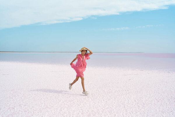 Woman in pink dress enjoying walking by serenity colorful landscape of salt flats on pink lake Stock Picture