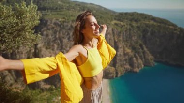 Yandan bakan mutlu gezgin özgürlüğü, açık kollarla kadını güldürüyor ve dağ manzarasından zevk alıyor, Türkiye 'nin Kelebek Vadisi' nde yaz tatili. Kız denizin üzerinde uçurumun tepesinde duruyor
