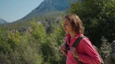 Sinematik 4k yavaş çekim çekici kadın yürüyüşçü dağlarda arka planda ormanla yürüyor, güneşli bir günde yürüyüş yapan mutlu bir kız, açık hava macera tarzı..