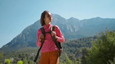 4k sinematik yavaş çekim. Çekici genç kadın yürüyüşçünün yakın plan portresi güzel dağ manzarasında duruyor. Güneşli bir günde açık havada yürüyüş yapan mutlu bir kız..
