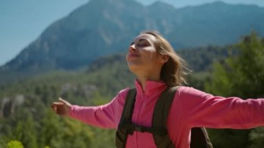 4k yavaş çekimde, güzel dağ manzarasında duran genç bir kadının yakın plan portresi, güneşli bir günde dışarıda yürüyüş yapan mutlu bir kız, açık hava macerası..