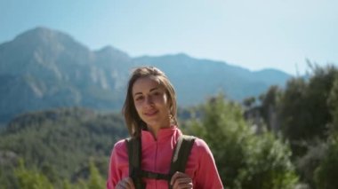 4k sinemada, gülümseyen kadın yürüyüşçünün güzel dağ manzarası üzerinde duruşu, güneşli bir günde rüzgarda esen saçları olan mutlu kız, açık havada macera dolu bir hayat tarzı..