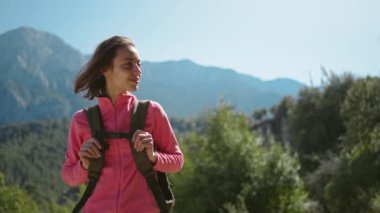 4k sinematik yavaş çekim. Çekici genç kadın yürüyüşçünün yakın plan portresi güzel dağ manzarasında duruyor. Güneşli bir günde açık havada yürüyüş yapan mutlu bir kız..