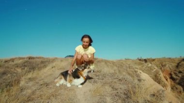 Güzel, mutlu ve sevecen, sarı elbiseli, sevimli Corgi köpeğiyle gülen bir kız sabah güneşiyle birlikte kil tepede oturuyor. Hayvanlarla seyahat etmek. Colal Ukrayna 'da, Stanislav kayalıklarında seyahat ediyor.