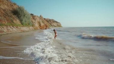 Bikini giymiş, rüzgârın ve dalgaların tadını çıkartan mükemmel ince vücut yapısı olan mutlu, neşeli kadının yavaş çekimleri. özgürlük ve tasasız, yaz tatili ve seyahat konsepti