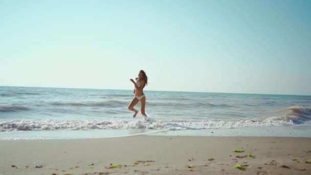 嵐の後波と海岸に沿って走る美しいフィットボディを持つ幸せな屈託のないスレンダーな女性 少女ジョギングや波を飛び越える 楽しい女の子は夏に屋外で楽しみます — ストック動画