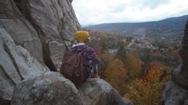 Kız yürüyüşçü uçurumun kenarında oturur ve uzaklığa, dağ manzarasına, seyahate ve spora bakar. Ukrayna 'daki ünlü turistik yer, Tustan Ulusal Parkı.