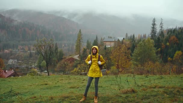 美しい秋の森の中でアクティブな健康的な女性のハイキング 黄色のレインコートで幸せな笑顔の若い女性の肖像画やハイキング休暇中の森林清掃の休息 — ストック動画