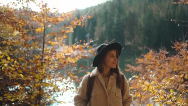 晴れた秋の日に秋の森の中を歩く陽気なウクライナ人女性観光客を閉じます 山の湖の周りの森の中でバックパックのハイキングと帽子の女性ハイカー寒い秋の朝 ウクライナのセイビア — ストック動画