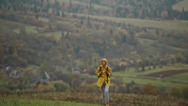 慢动作 启发了年轻漂亮的女徒步旅行者 她身穿黄褐色的雨衣 背着背包 头戴针织贝尼帽 在大自然的山丘上散步 享受着乌克兰的自然美景 — 图库视频影像