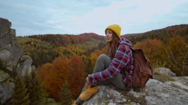 Sırt çantalı sarı bereli ve gündelik giyinen kadın gezgin uçurumun kenarında oturuyor ve güzel manzara, dağ manzarası, seyahat ve spor sunuyor. Ukrayna, Tustan 'da popüler bir turistik yer.