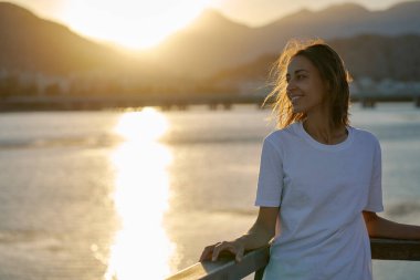 Turuncu gökyüzü ve güneş ışığıyla gün batımı manzarası. Dağları ve deniz manzarasını seven mutlu bir kadın. Akıl sağlığı doğa terapisi.