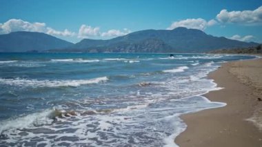 waving sea with waves at sunny summer windy day at beautiful sandy empty beach Iztuzu in Turkey. beautiful mountain range on background