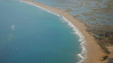 Türkiye 'nin güzel kumlu ve boş plajı Iztuzu' da güneşli yaz rüzgarlı bir günde dalgalarla dalgalanan hava ağır çekim. Arka planda güzel dağ sıraları