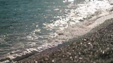 Yavaş çekim okyanus dalgaları öğleden sonra çakıl taşlı plajda yuvarlanır. Güneş suyun üzerinde parlar ve ıslak çakıl taşları. Seçici odaklanma, yaz havası, doğa güzelliği.