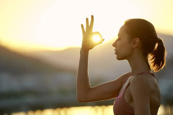 Side portrait close up face woman practicing yoga and meditation during sunset against mountain range. Girl makes mudra gesture with sunlight