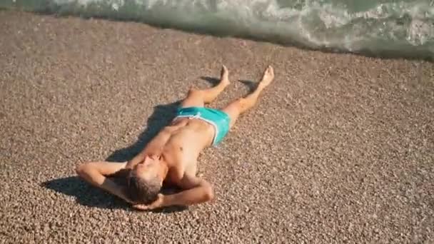 Handsome Athletic Man Blue Swim Trunks Relaxing Lying Pebble Beach — Vídeo de stock